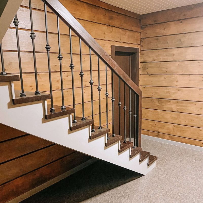 Г-образная деревянная лестница из ясеня с ковкой в брусовом доме