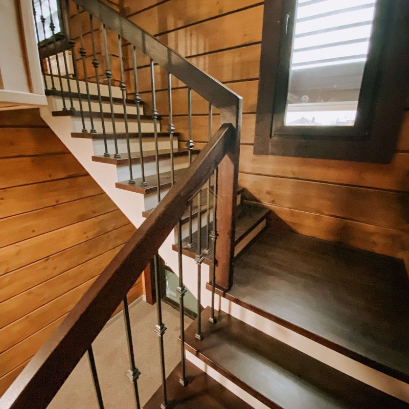 Г-образная деревянная лестница из ясеня с ковкой в брусовом доме