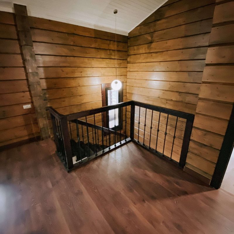 Г-образная деревянная лестница из ясеня с ковкой в брусовом доме