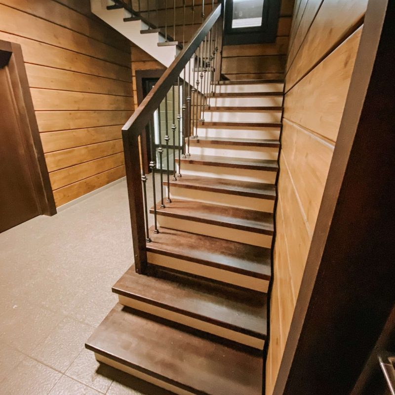 Г-образная деревянная лестница из ясеня с ковкой в брусовом доме