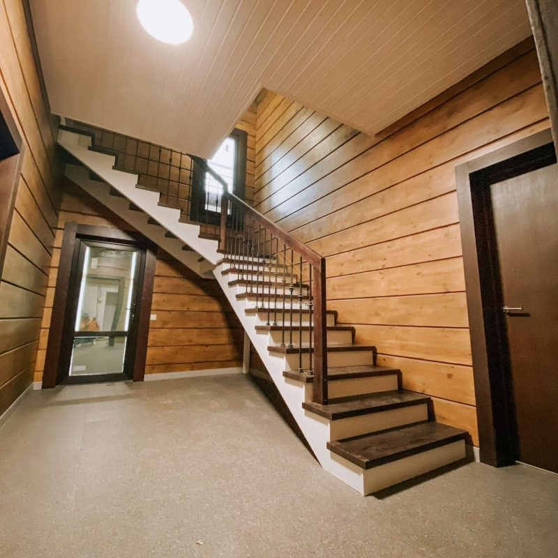 Г-образная деревянная лестница из ясеня с ковкой в брусовом доме